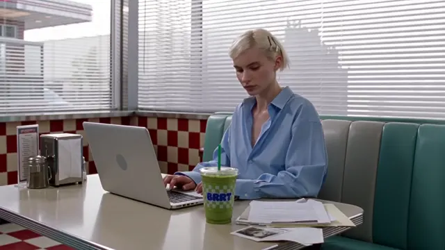 Woman working on a laptop at a desk in front of a diner-style backdrop