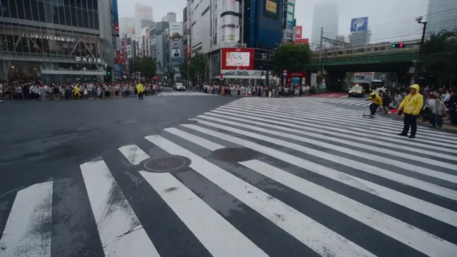 Pedestrians crossing a broad city intersection framed by tall buildings